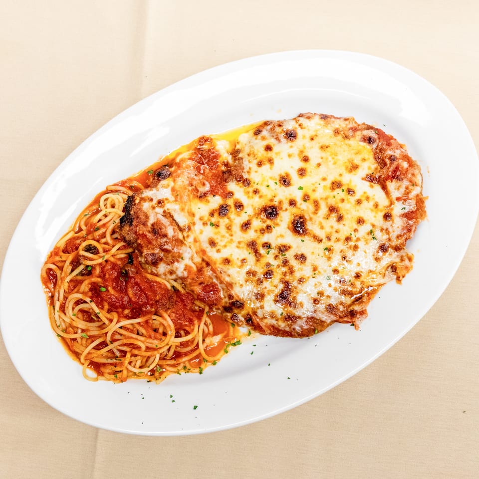 Baked chicken parmesan topped with melted mozzarella, served alongside spaghetti in tomato sauce on a white plate.