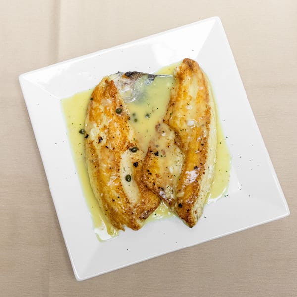 Three grilled fish fillets topped with lemon butter sauce and capers on a white square plate.