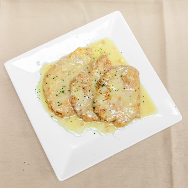 Golden-brown breaded chicken cutlets topped with lemon butter sauce and parsley on a white square plate.