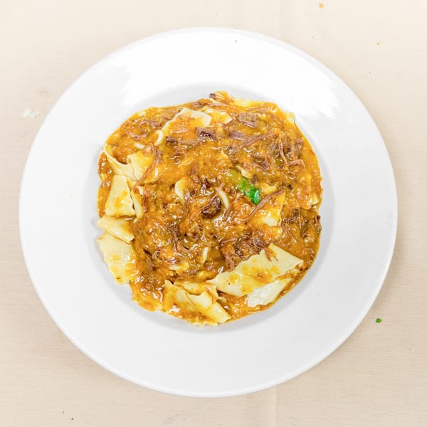Plate of pasta topped with shredded meat in a rich orange sauce, garnished with green herbs.
