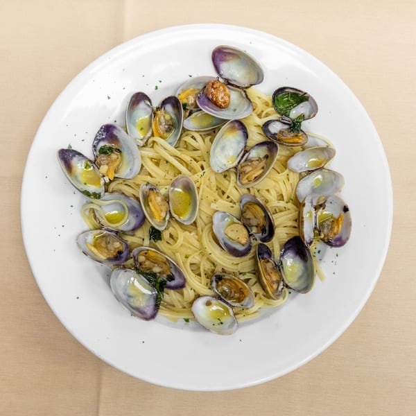 Plate of linguine topped with open clams, garlic, herbs, and olive oil on a beige tablecloth.
