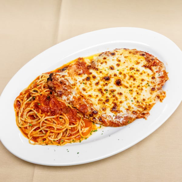 Cheesy chicken Parmesan with tomato sauce and spaghetti, garnished with parsley, served on a white plate.