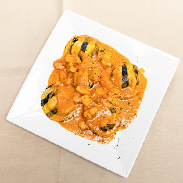 Grilled shrimp and vegetables served in a creamy orange sauce on a white square plate.