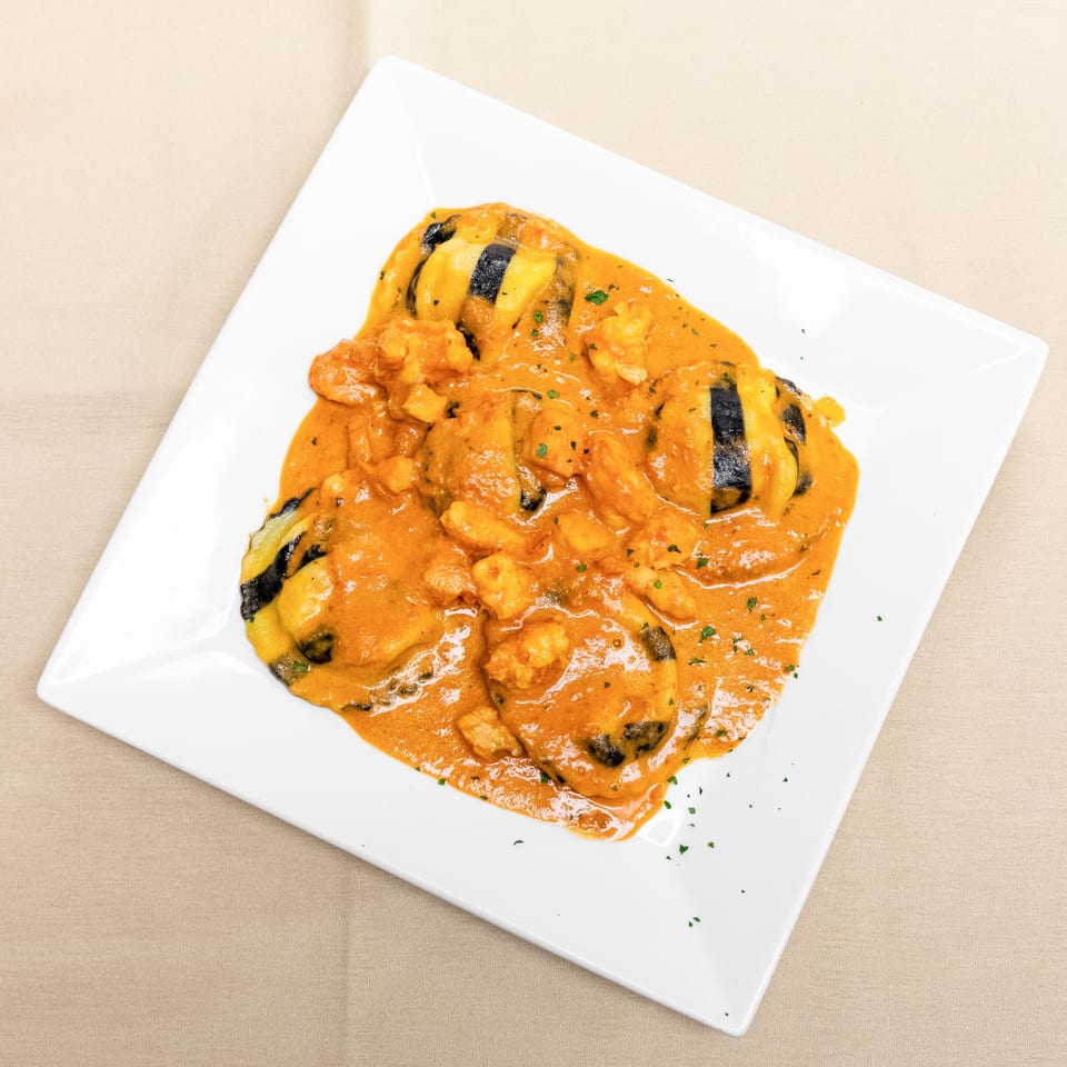 Grilled shrimp and vegetables served in a creamy orange sauce on a white square plate.