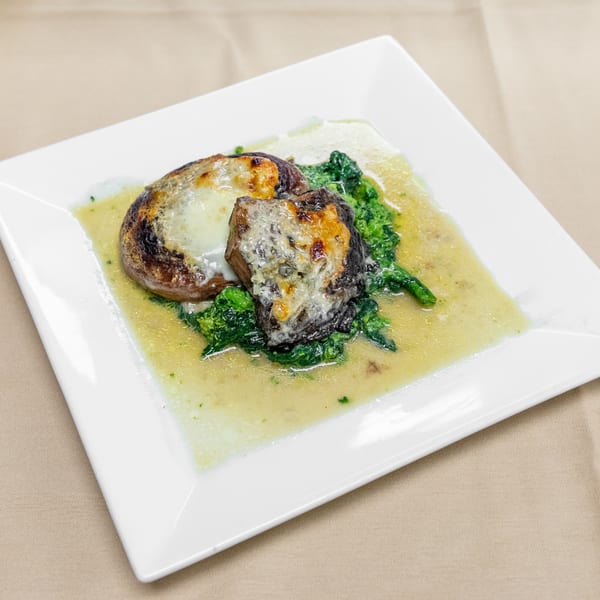 Two grilled portobello mushrooms topped with melted cheese, served over sautéed greens in a light sauce on a white plate.