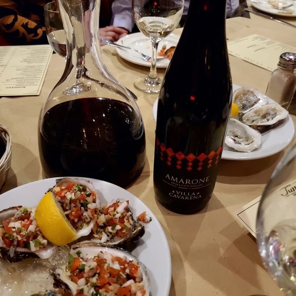 A table set with oysters, a decanter of red wine, and a bottle of Amarone Villa Cavarena.