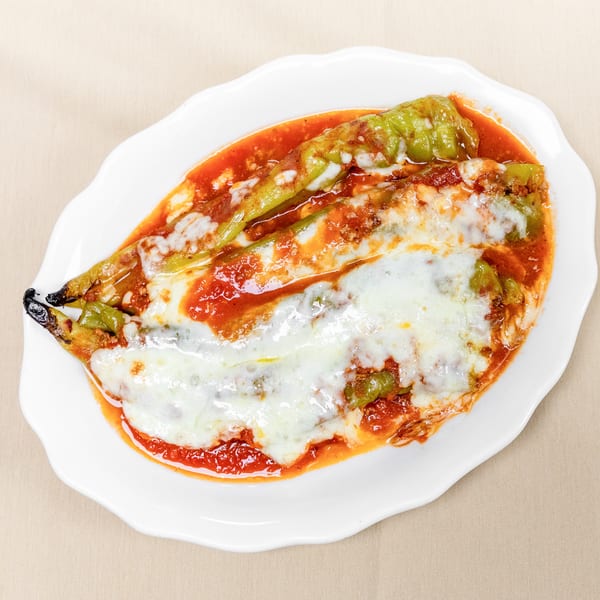 Roasted green peppers topped with melted cheese and tomato sauce on a white plate.