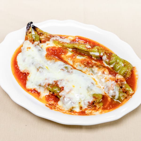 Roasted green peppers topped with melted cheese and tomato sauce on a white plate.