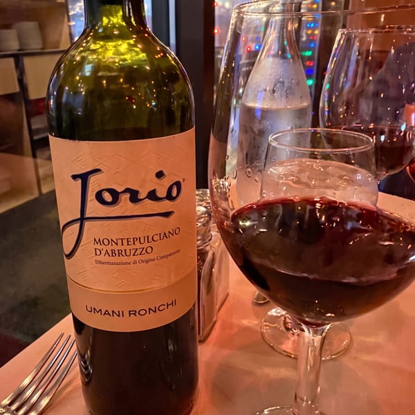 A bottle of Jorio Montepulciano d'Abruzzo wine next to a glass of red wine on a restaurant table.