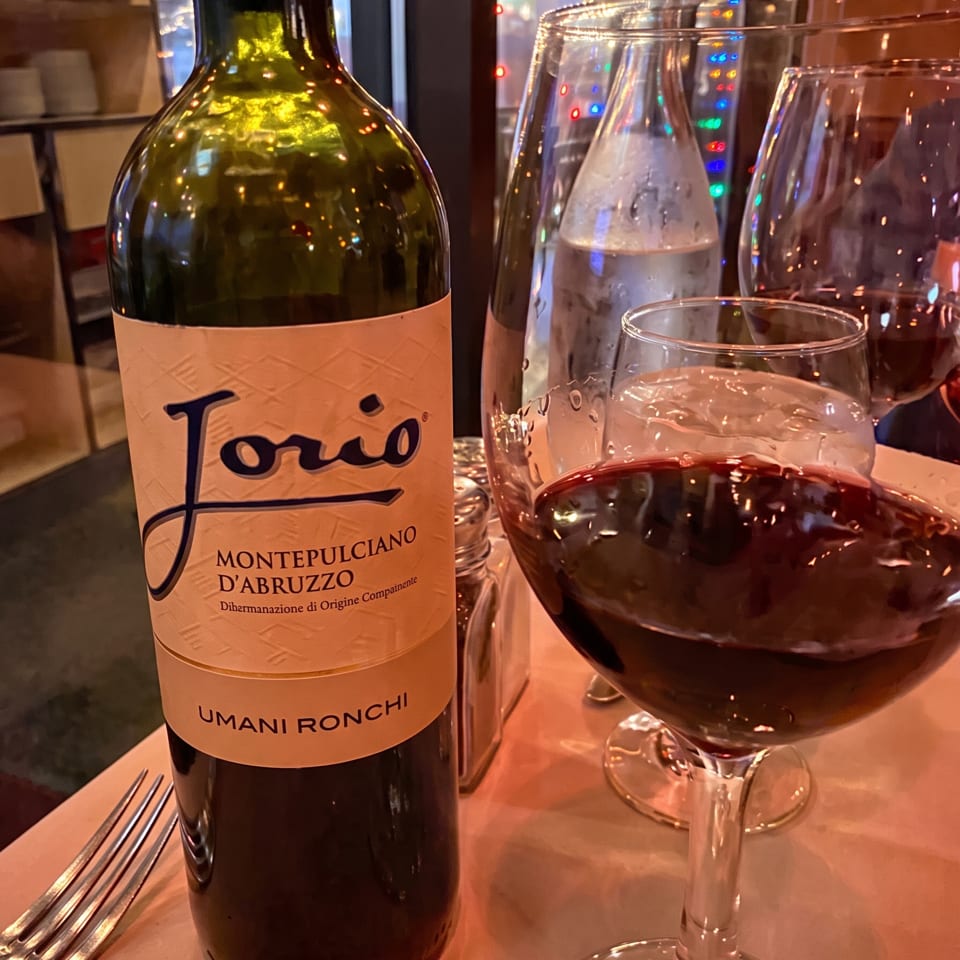 A bottle of Jorio Montepulciano d'Abruzzo wine next to a glass of red wine on a restaurant table.
