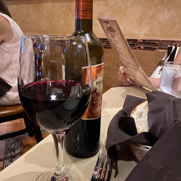 A glass of red wine and a bottle of Las Pirineos wine on a table with bread and a menu.